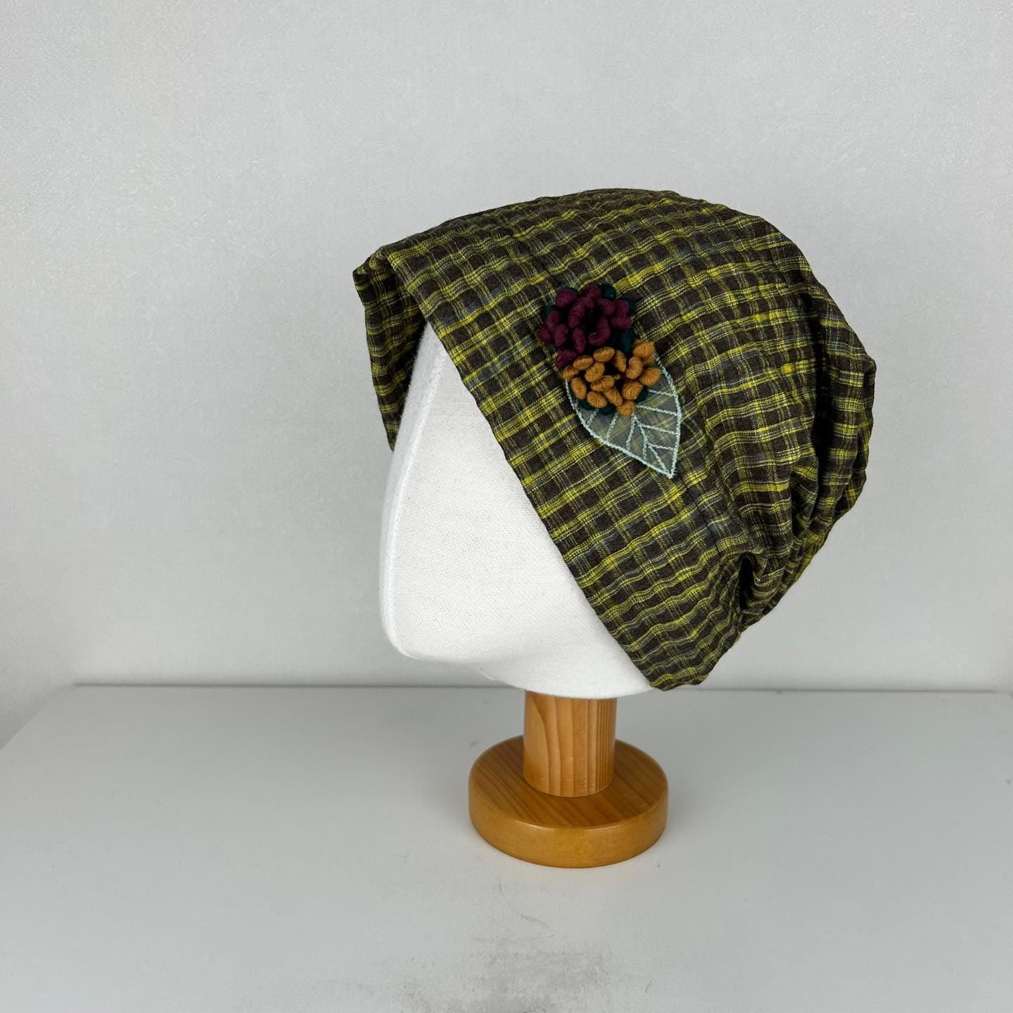 Olive and brown checkered beanie with decorative flower and leaf embellishment on a mannequin head