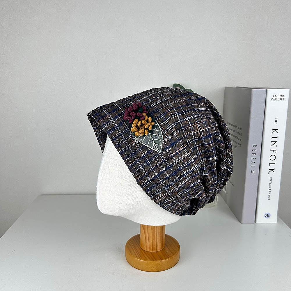 CHEKERED BEANIE: Plaid beanie hat with a floral appliqué, displayed on a mannequin head.