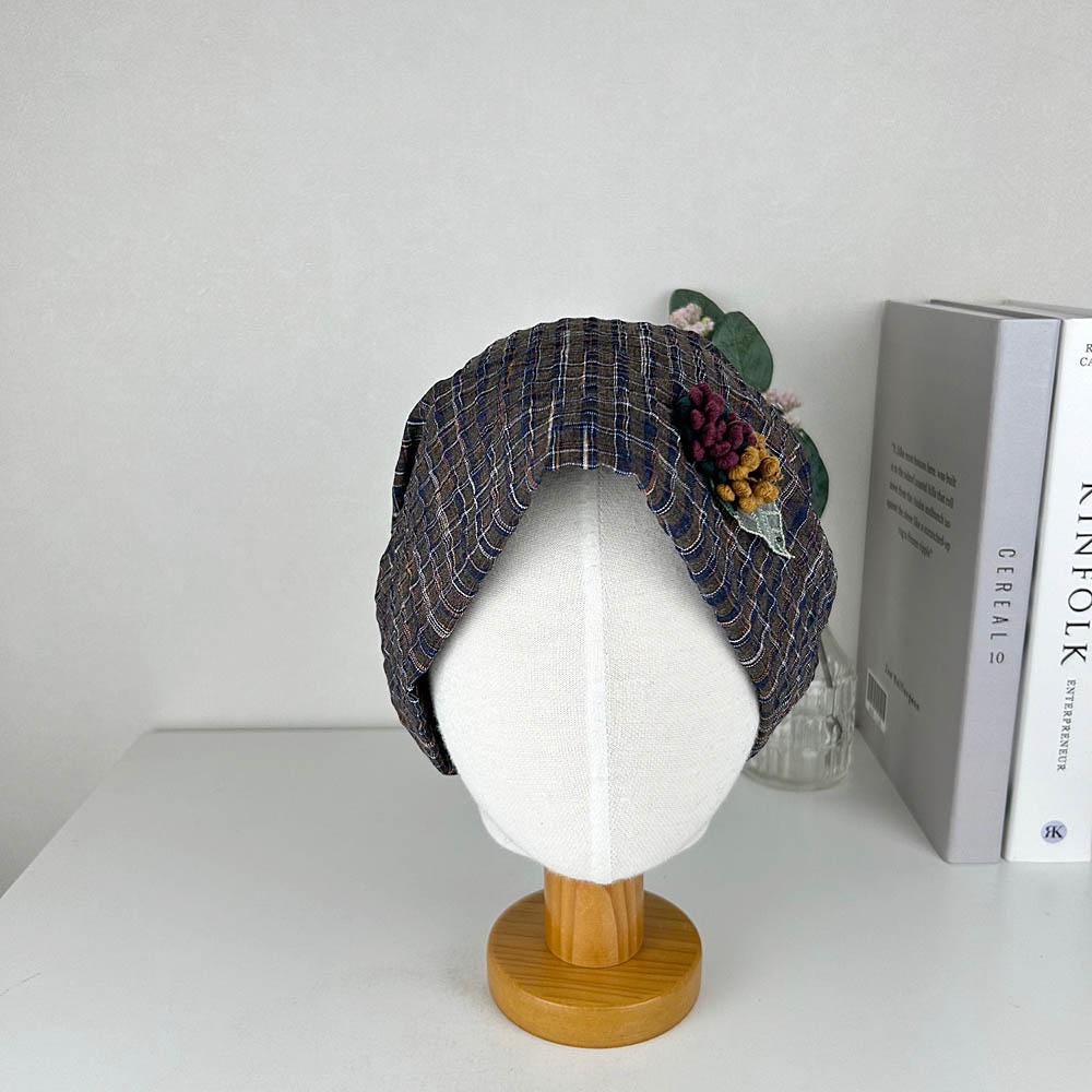 CHEKERED BEANIE: Brown and blue plaid hat with floral embellishment on a mannequin head.