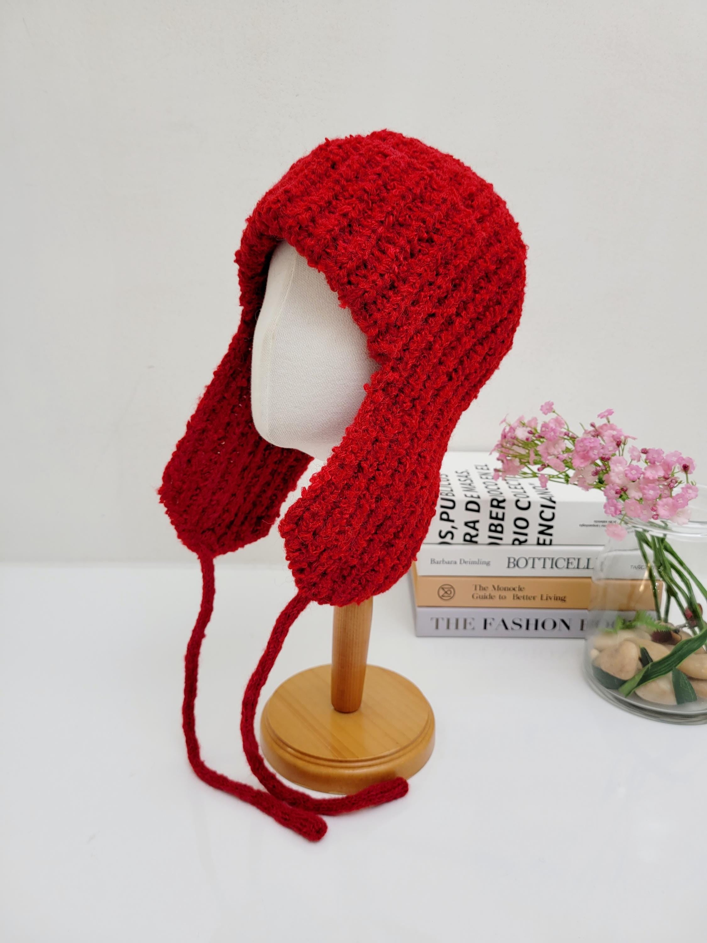 Red knitted wool earflap hat on a mannequin. The hat features long ties and a textured knit, perfect for winter warmth and style.
