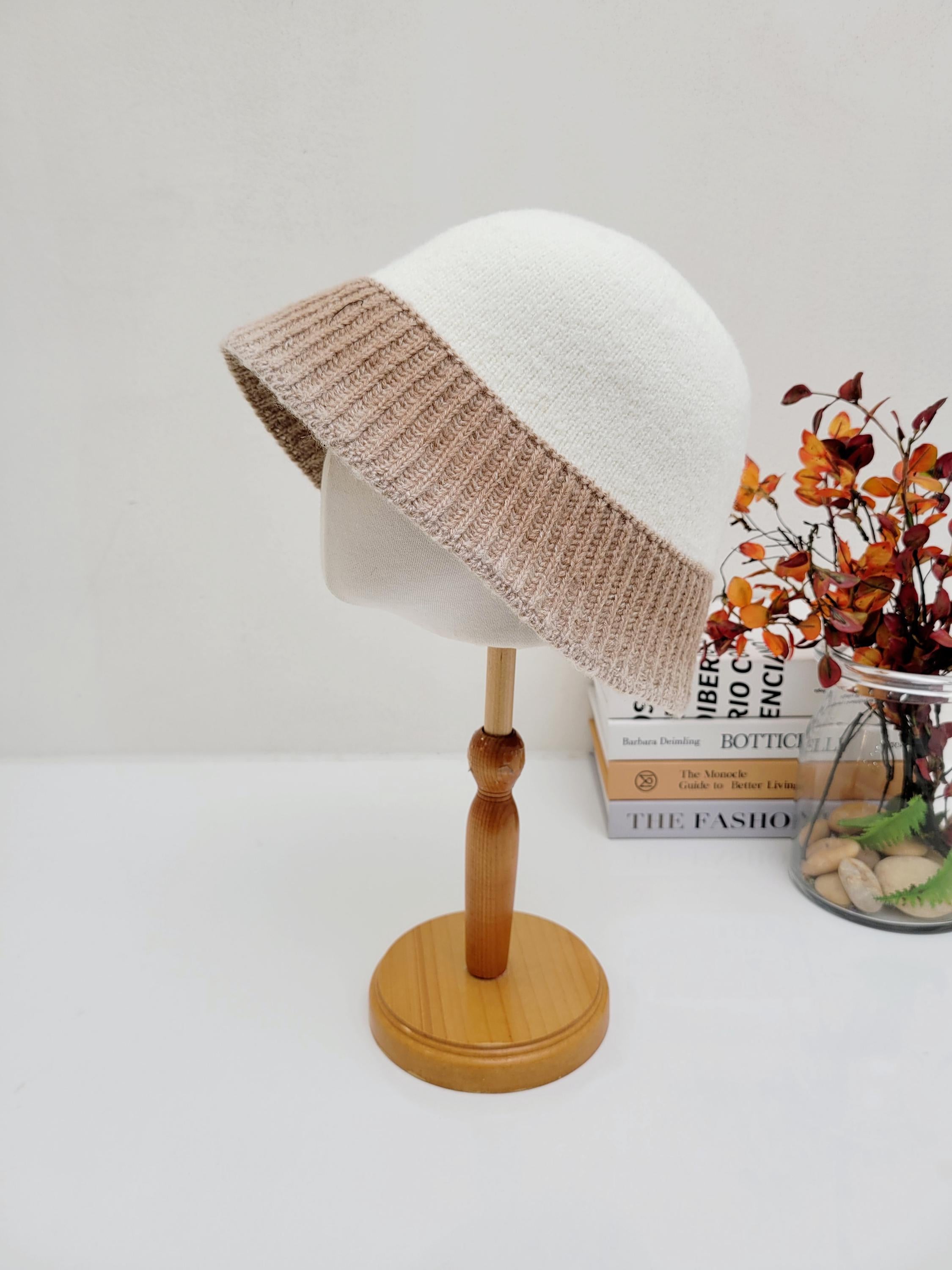 diana hat: A cozy white knitted hat with a tan ribbed brim, displayed on a wooden stand.