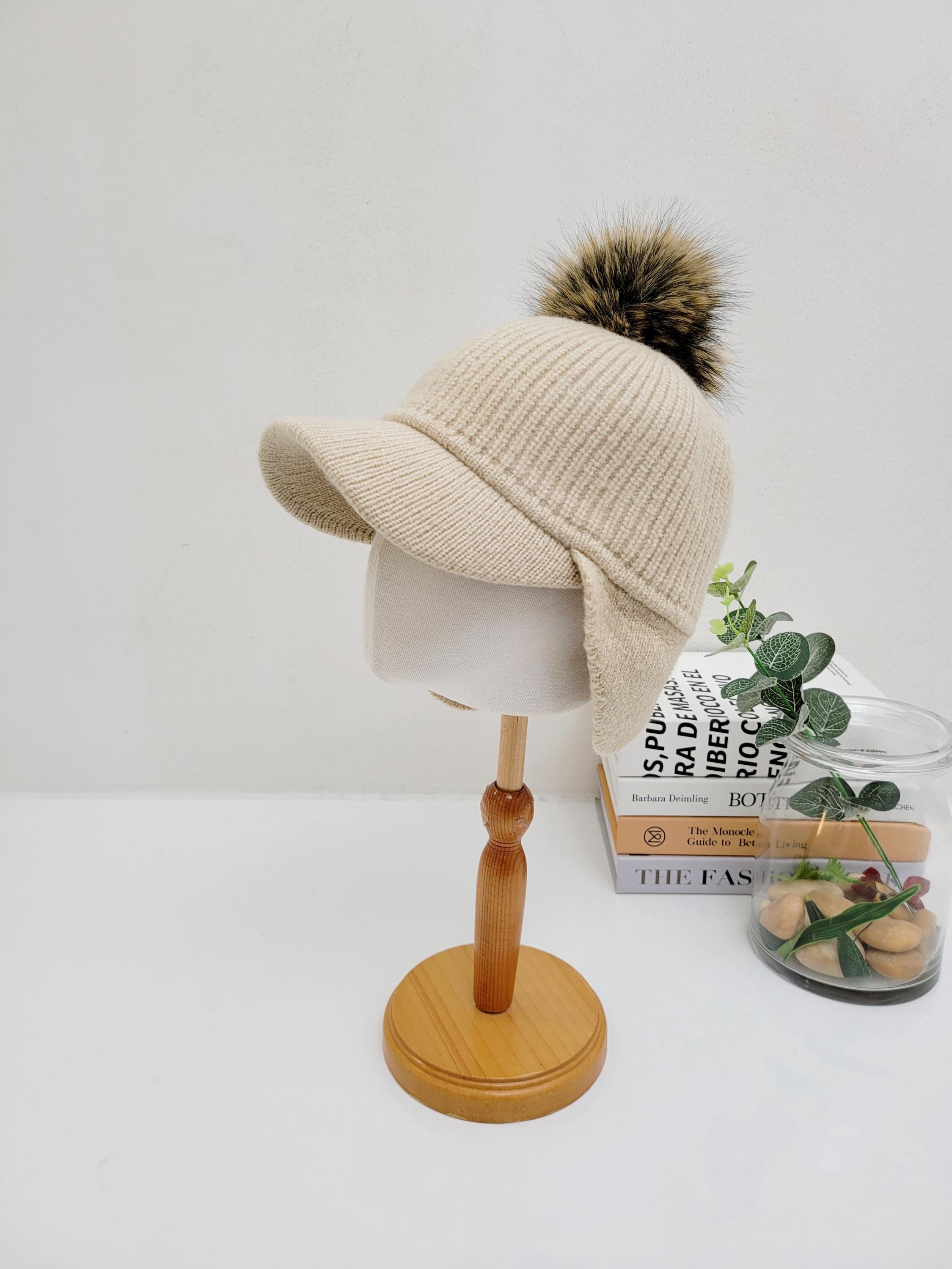 Beige ribbed cap - pom with ear flaps and faux fur pompom, displayed on a wooden stand