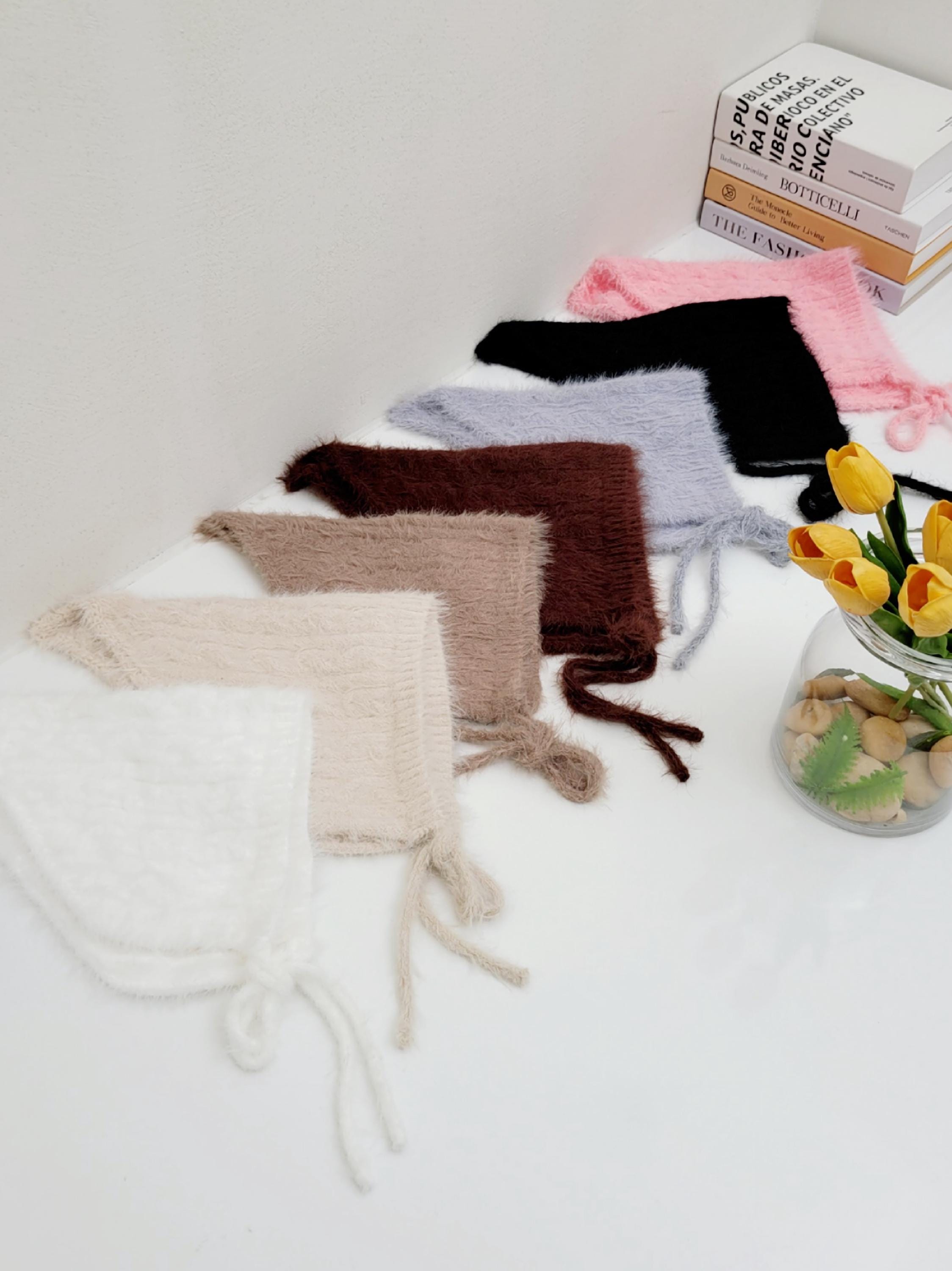 little riding hood bonnets in cream, beige, brown, light blue, black, and pink. Soft, fuzzy texture with tie closures.