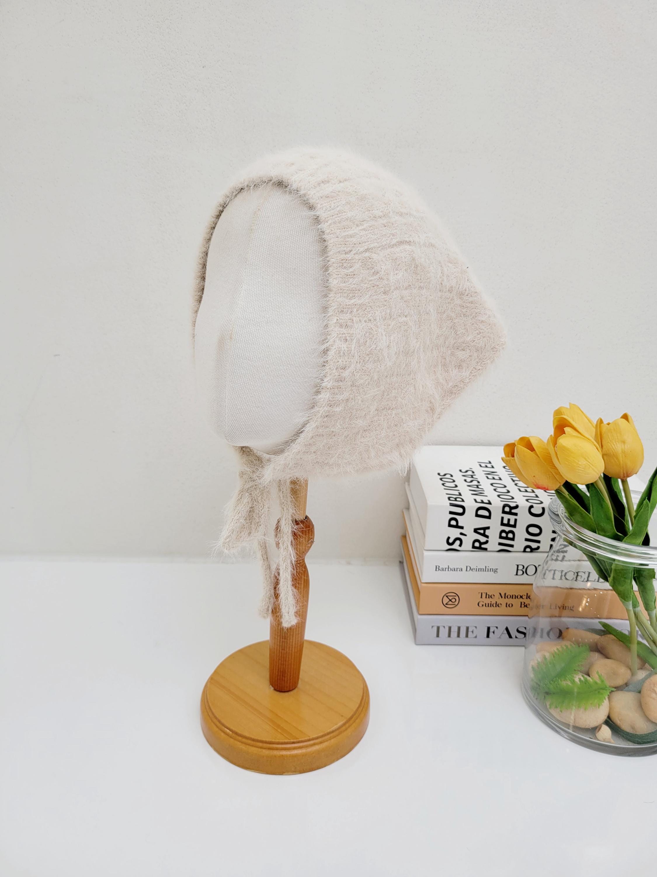 Beige fuzzy knit bonnet, the little riding hood, with tie strings, displayed on a mannequin head.