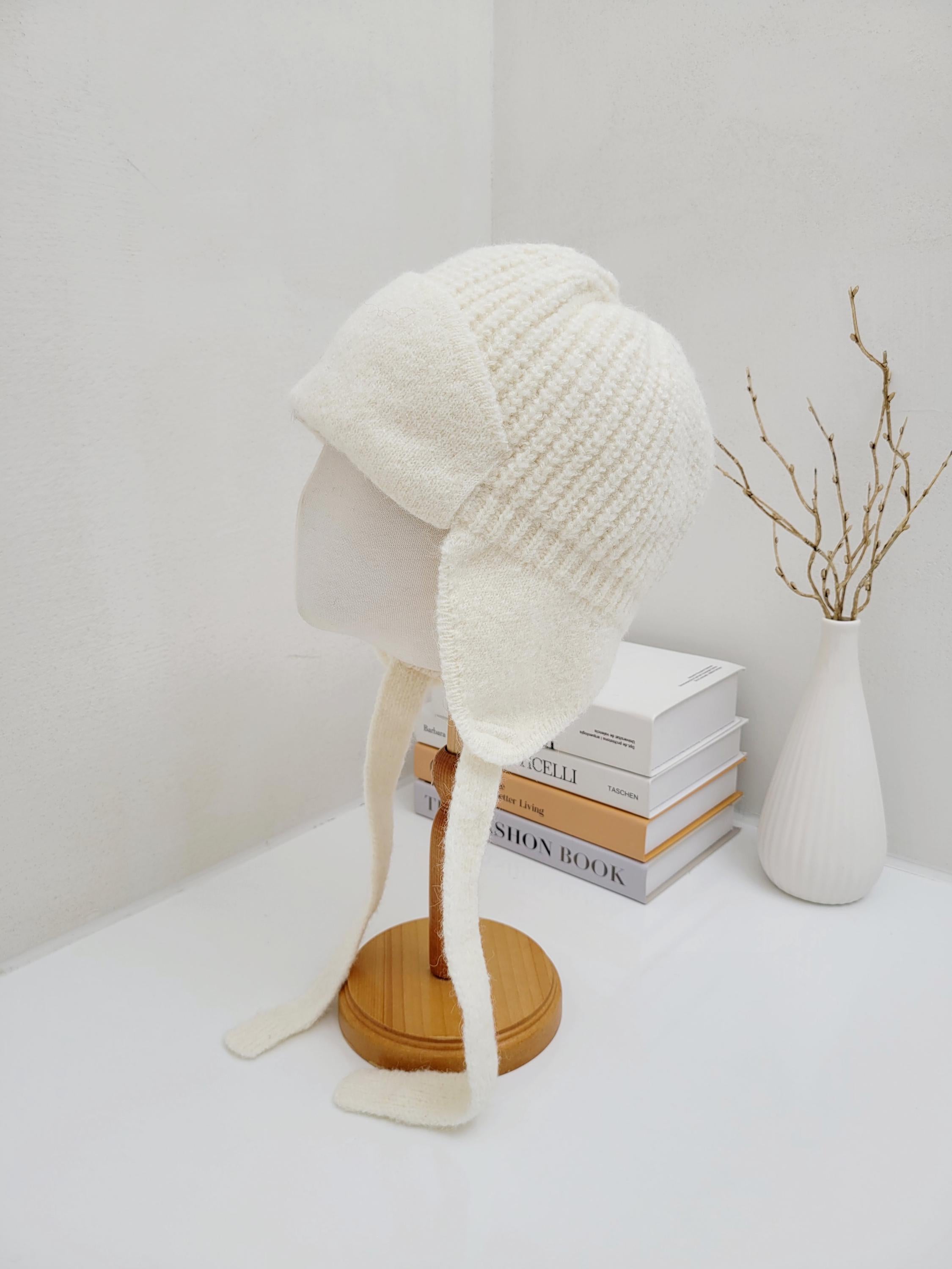 Cream knit amelia trapper hat with ear flaps and tie details, displayed on a mannequin head.