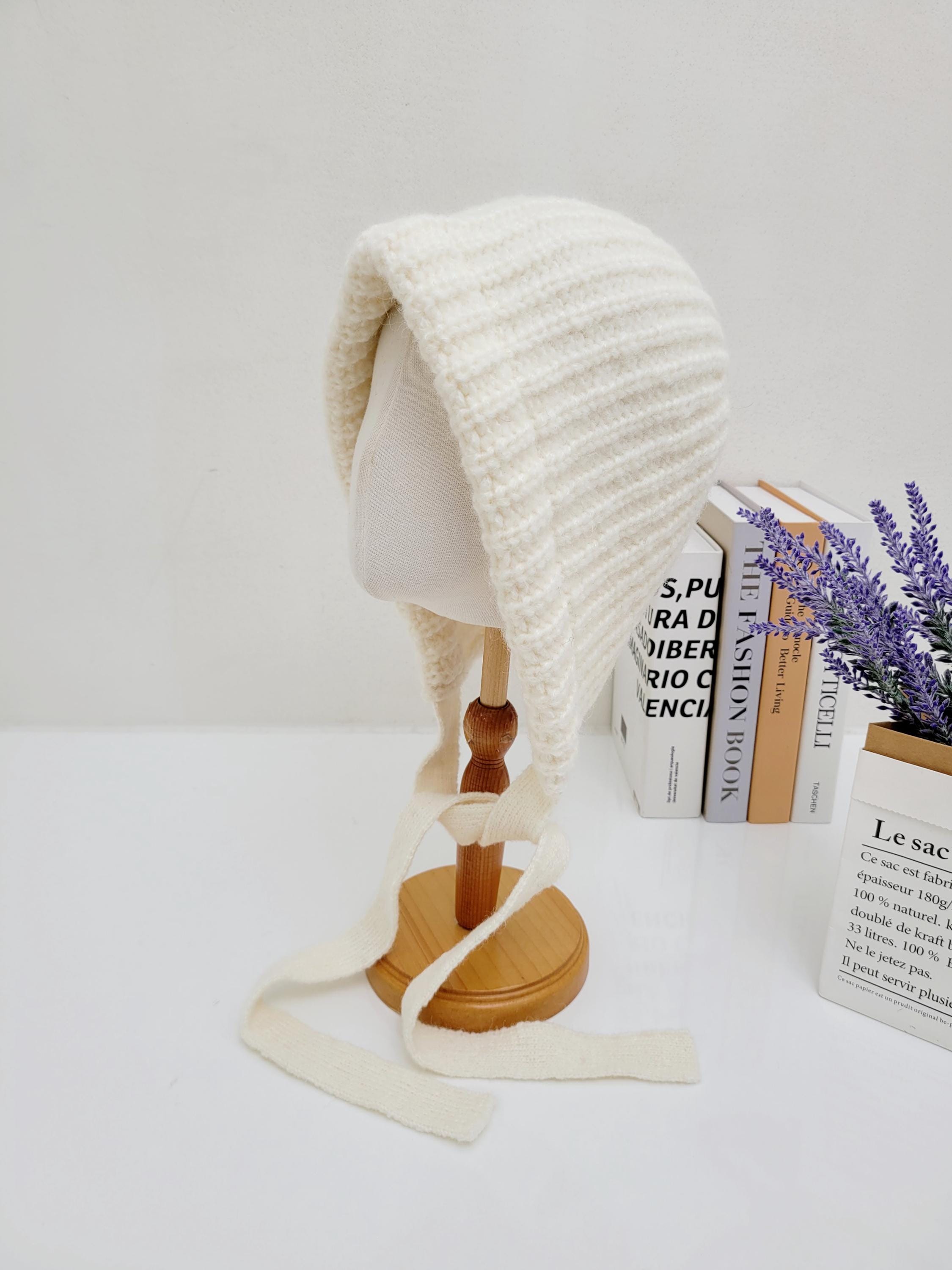 Creamy knitted bonnet from tour le jour, shown on a mannequin head. Features a cozy texture and tie closures for a secure, adjustable fit.