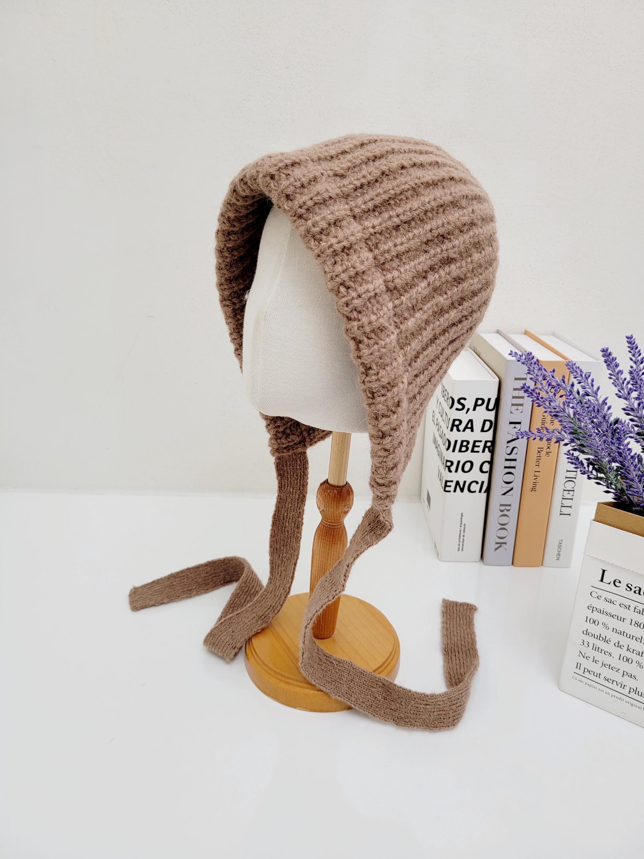 Brown knit bonnet, a tour le jour design, on a mannequin head, featuring long, soft ties.