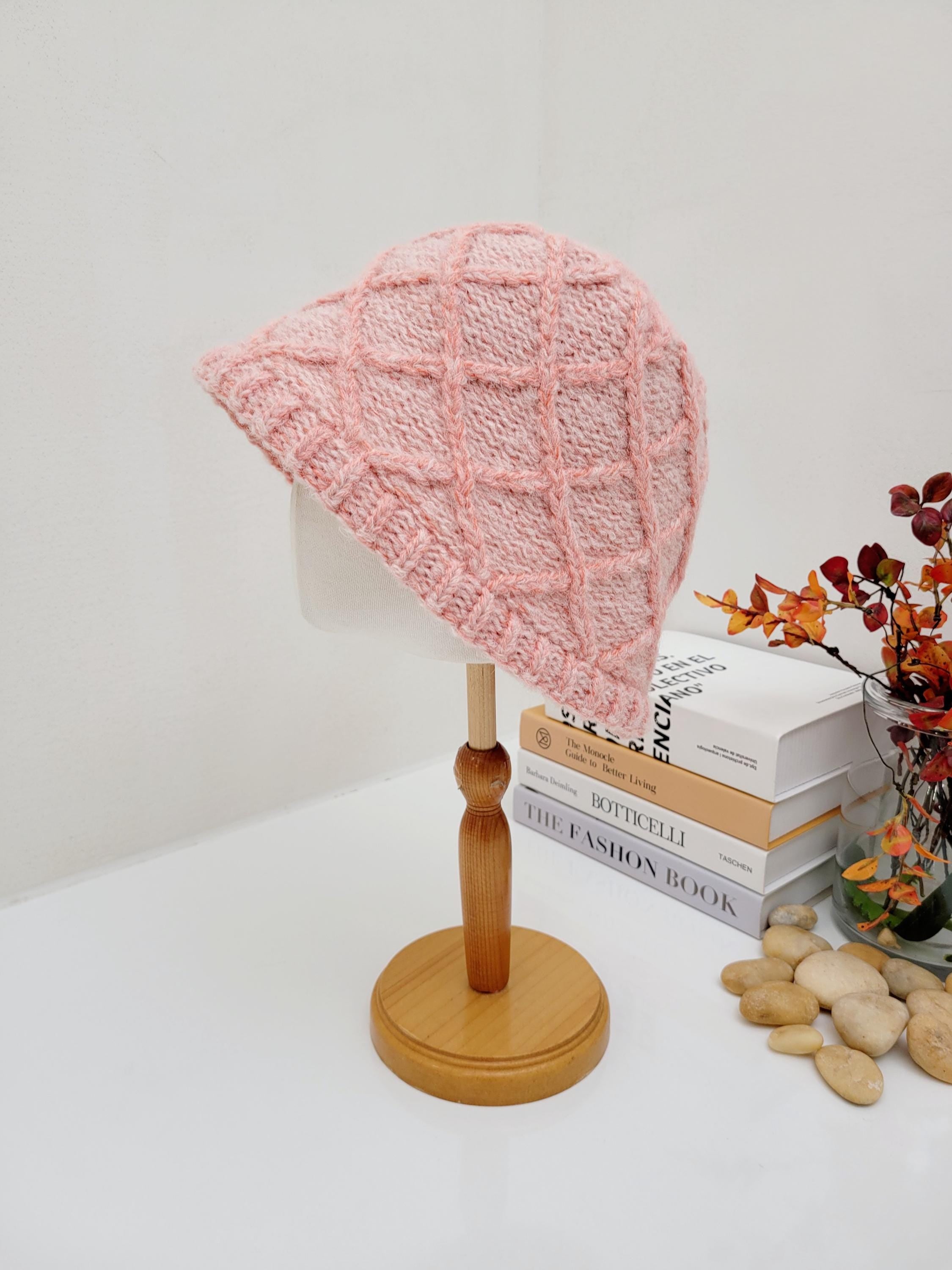 Pink knitted "winter in the paris" hat with a textured diamond pattern, displayed on a wooden stand.