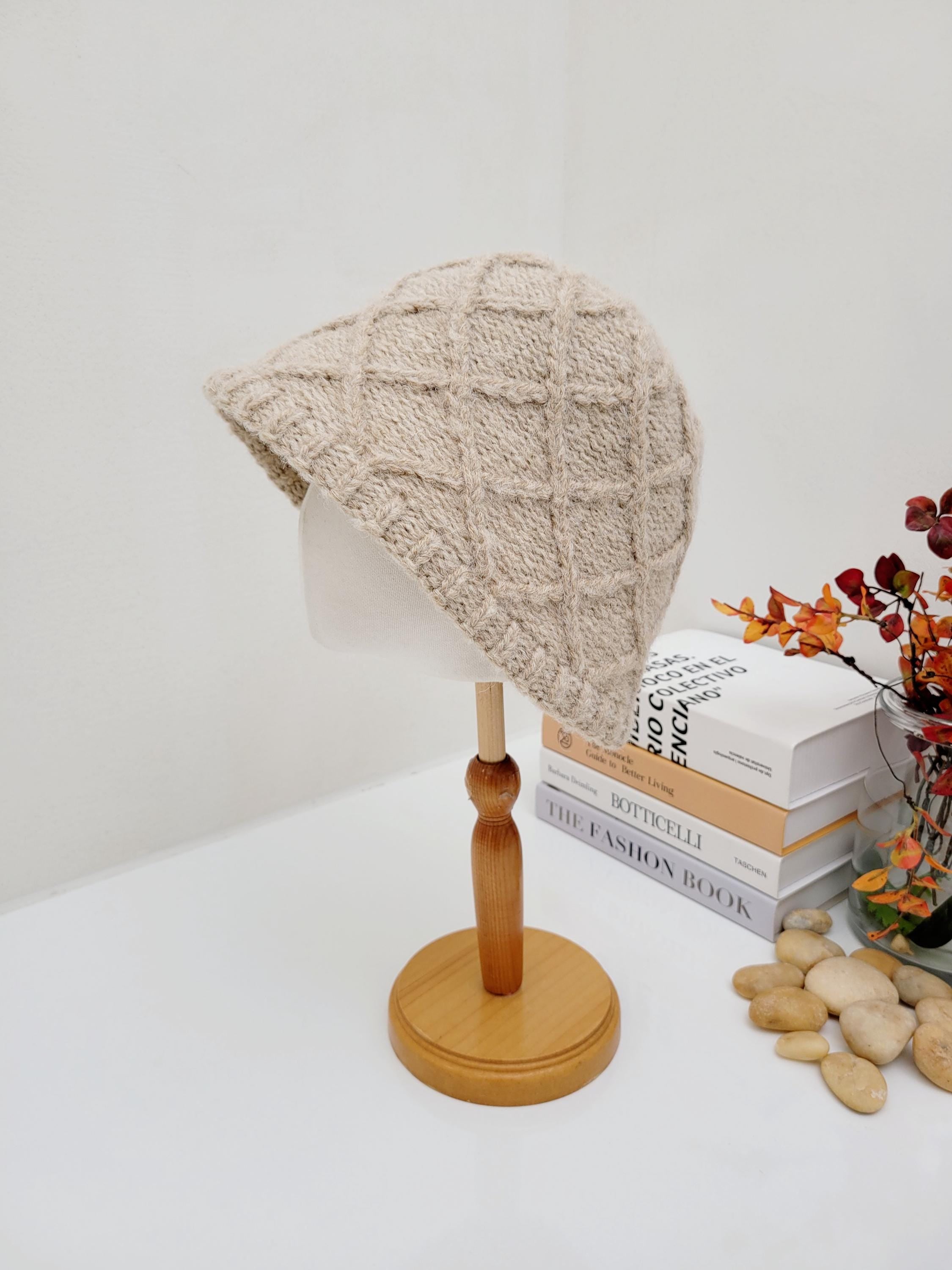 Beige knit winter in the paris hat with a textured diamond pattern, displayed on a wooden stand.