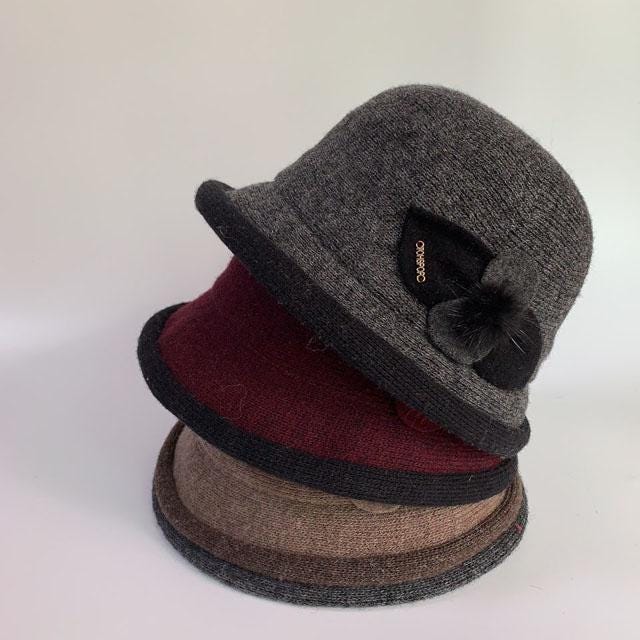 Stack of linda's favorite cloche hats in gray, burgundy, and brown. Each hat features a dark trim and a small flower detail.