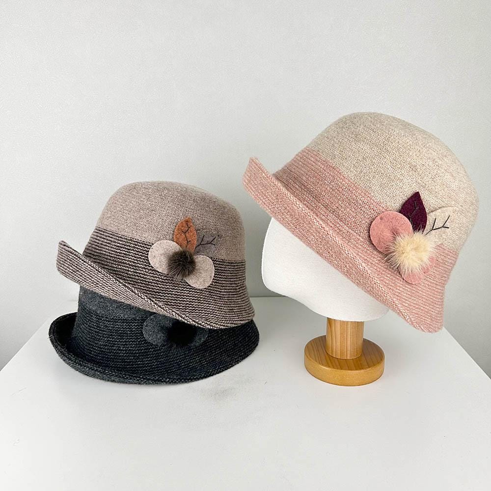 Three catherine cloche hats: brown, pink (on stand), and black. Each hat features a flower detail and a classic cloche shape. 