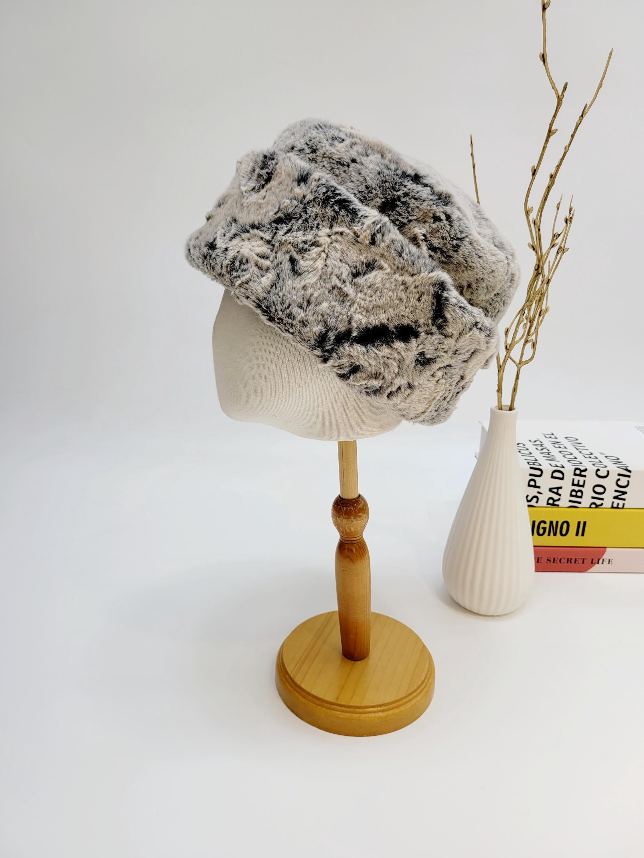 Fuzzy grey and black fake fur russian hat displayed on a wooden stand, blending warmth and style. A cozy and fashionable headwear choice.