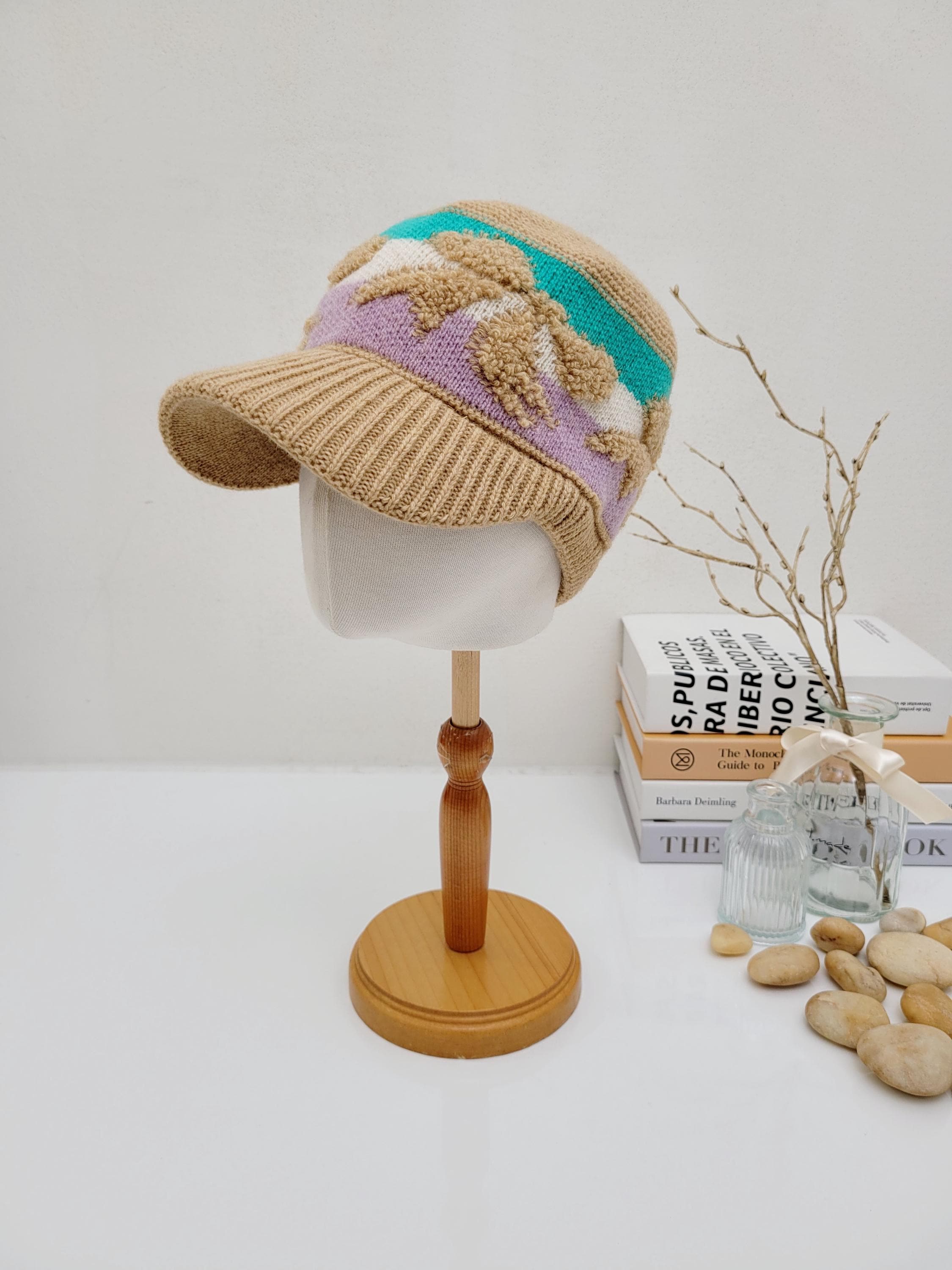 Tan earmuff knitted wool cap with lavender, cream, and teal accents, displayed on a mannequin head