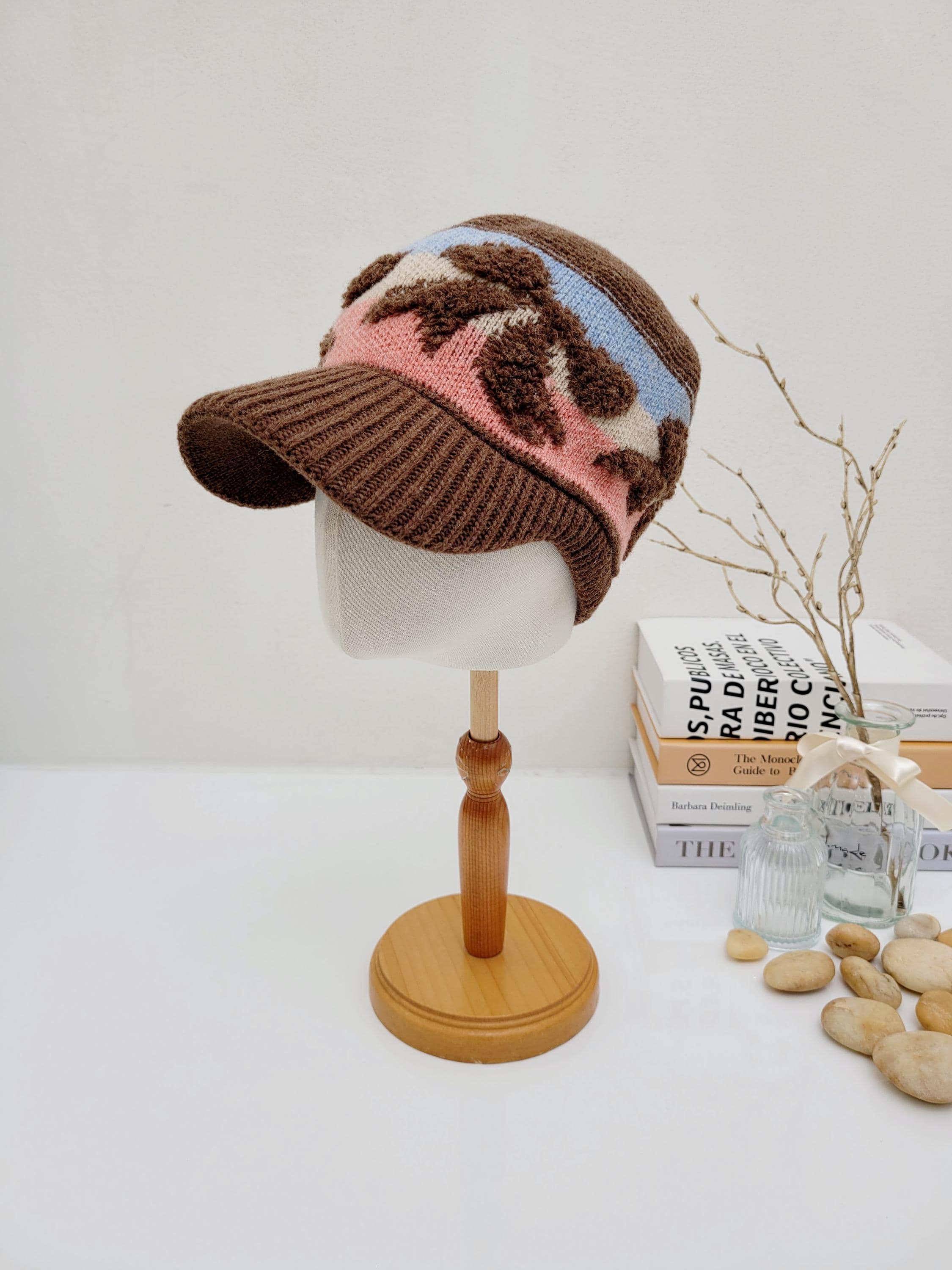 EARMUFF KNITTED WOOL CAP: Brown knit cap with brim, a pink and blue floral band, and ribbing, displayed on a mannequin.