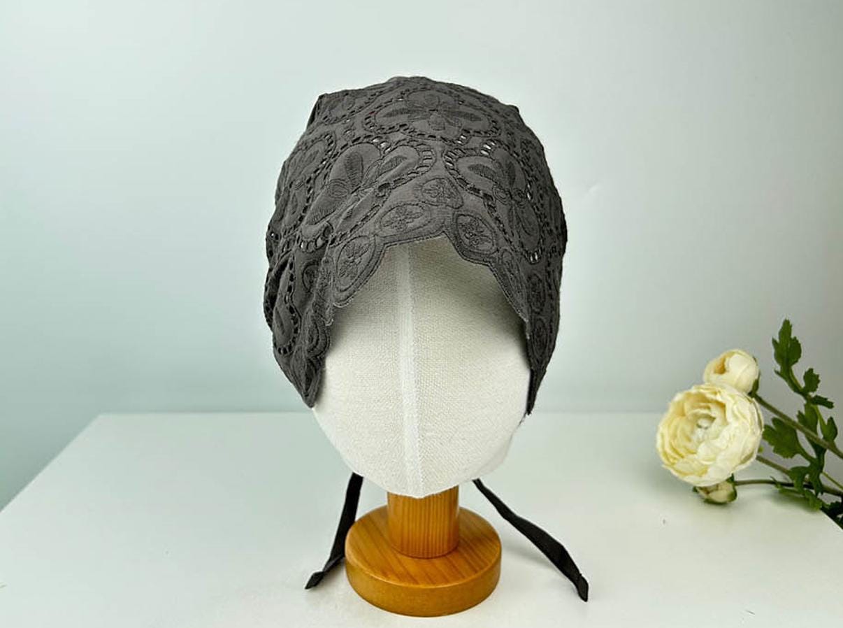 Gray eyelet beanie on a mannequin head. Lace detailing and ties add a vintage touch to this soft head covering.