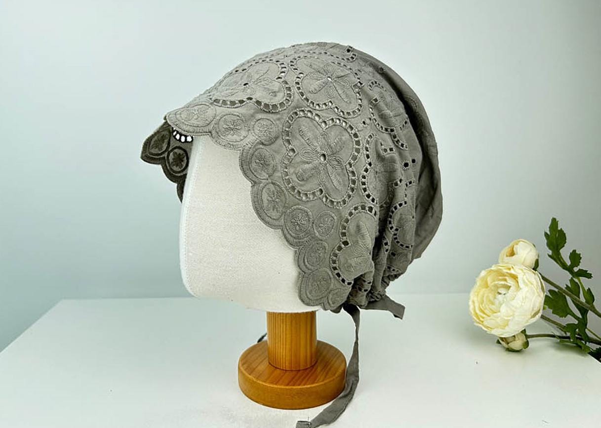 Gray eyelet beanie featuring delicate floral cutouts and tie strings, displayed on a mannequin head.