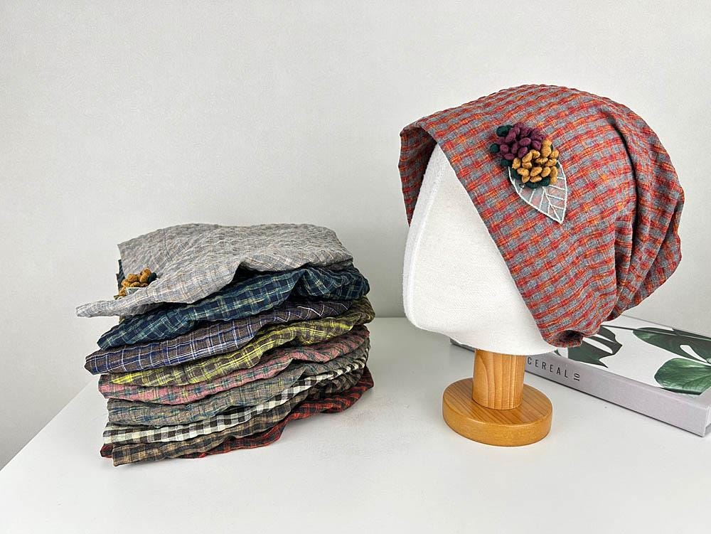 Stack of checkered beanies in various colors, and one displayed on a mannequin head. The chekered beanie has a floral embellishment.