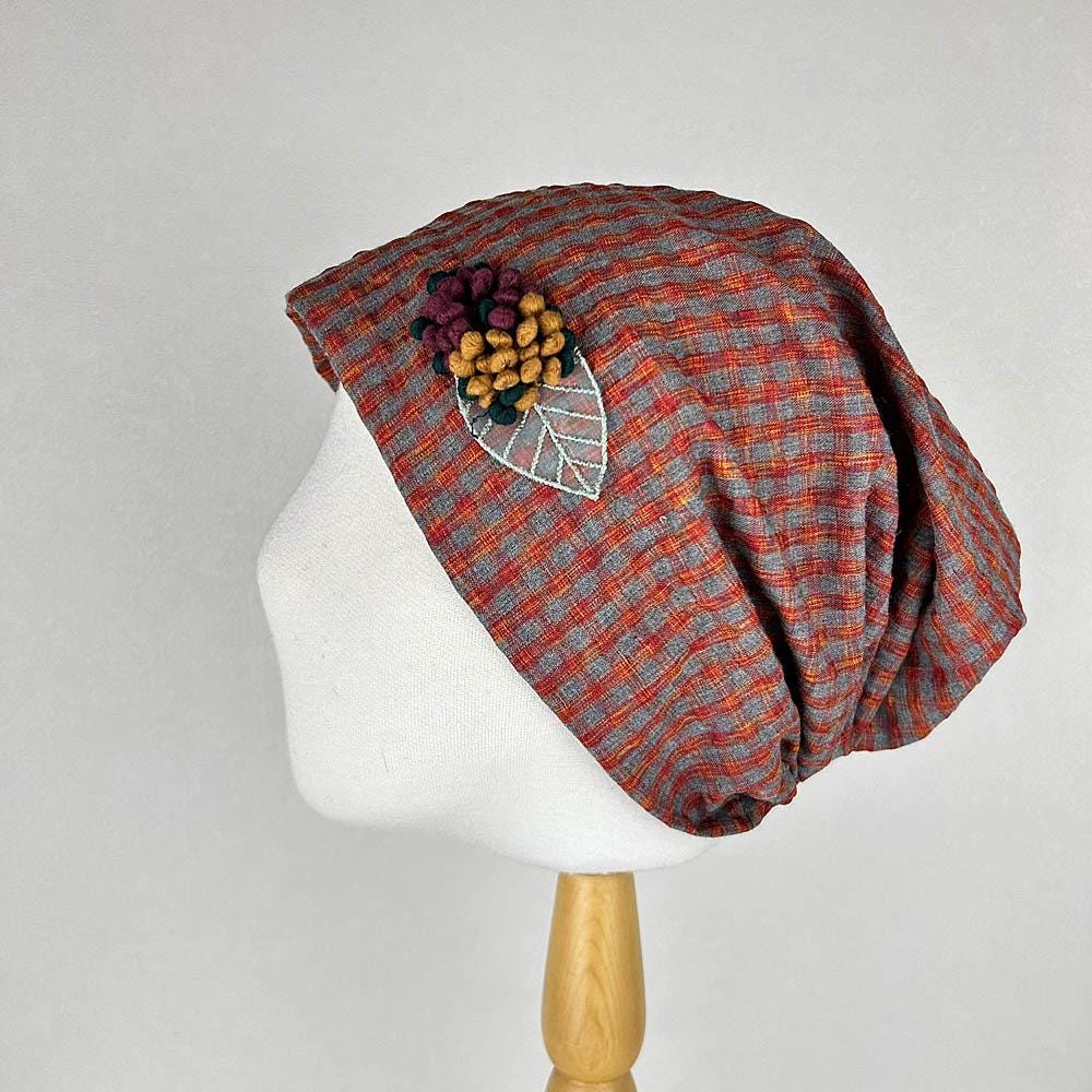 Red and grey checkered beanie with floral embellishment, displayed on a mannequin head