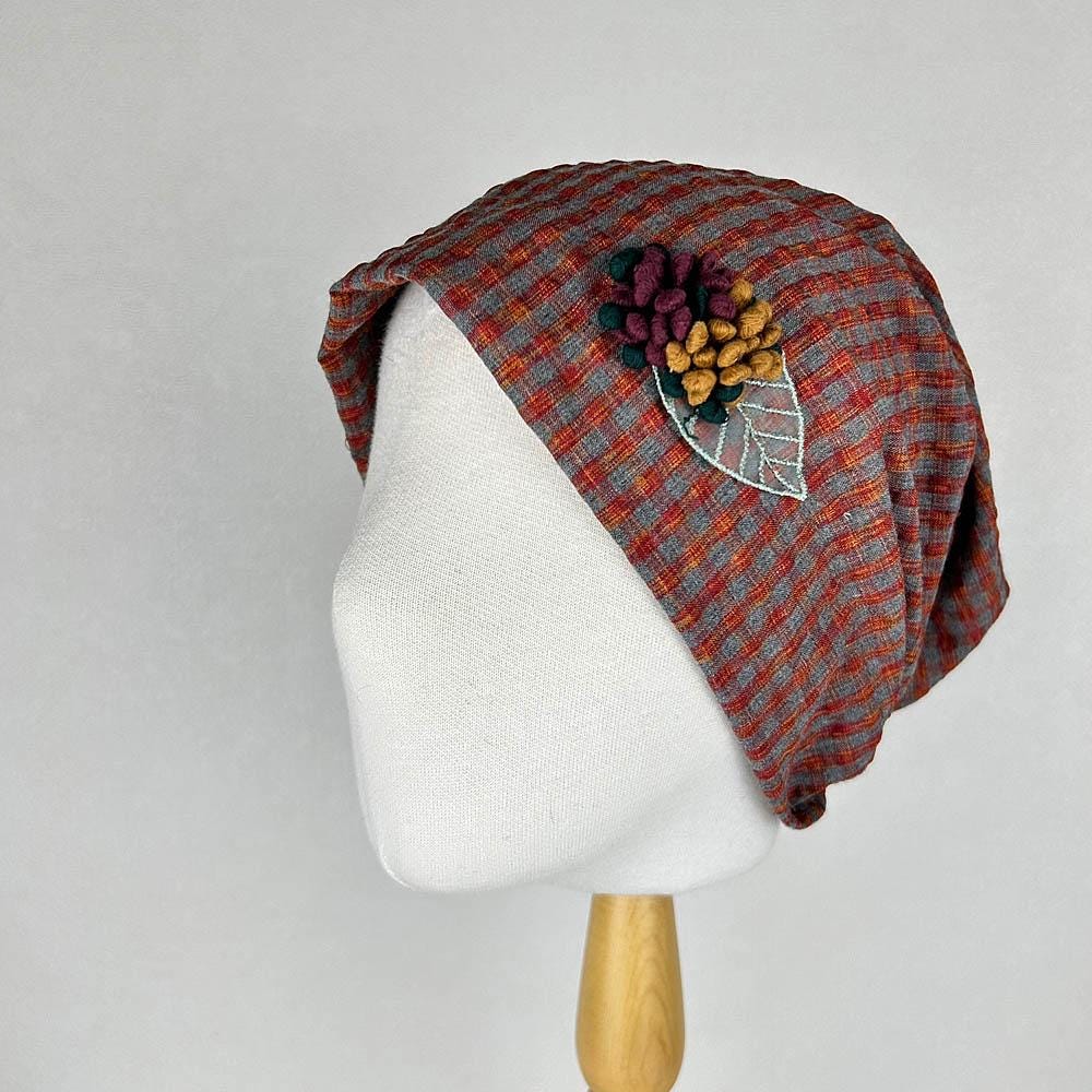 Red and gray checkered beanie with a floral applique featuring burgundy, yellow, and green accents